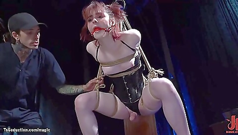 Sexy redhead in a red bondage suit is being hanged